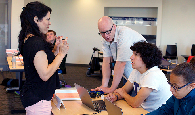 A student looks to an interpreter while the educator shows him how to design a website.