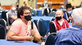 A participant sitting at a table speaks into the mic to ask a question during a session at Tapia 2023.