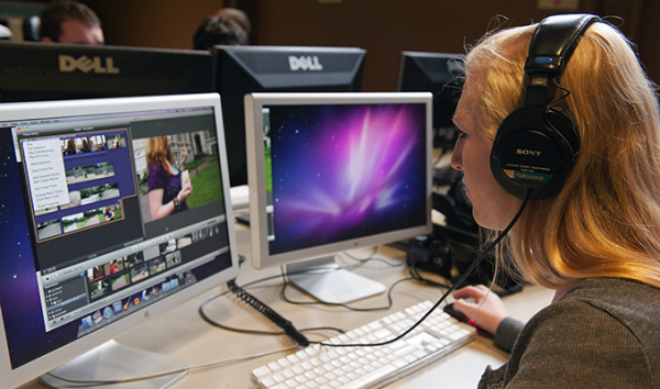 A student using headphones works on video editing on her computer