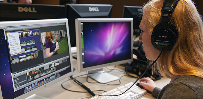 A student using headphones works on video editing on her computer