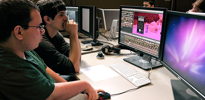 A student with a disability works with an educator to edit a video on a desktop computer